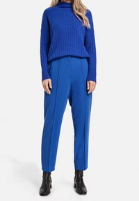 Blå ribbad polokrage tröja i kombination med strukturerade blå byxor med veck; avslutad med svarta ankelskor.