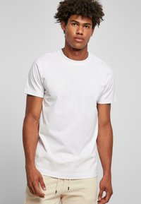 Tricou alb din bumbac cu guler rotund și mâneci scurte, având o textură simplă și un croi lejer, asortat cu pantaloni bej cu șnur.