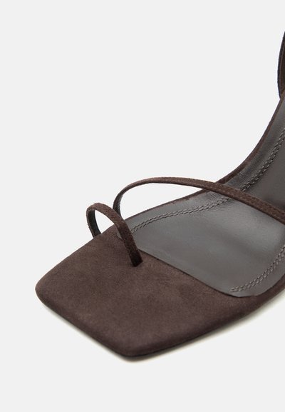 Sandale en daim marron foncé avec un bout carré, dotée d'une fine bride en boucle sur les orteils et d'une sangle étroite traversant le pied.