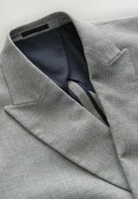 Col revers en blaser texturé gris avec une doublure contrastante bleu foncé. Présente des revers à cran et un détail de couture complexe sur le devant.