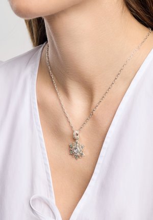 Sølv halskæde med en snefnugsformet vedhæng, der har flere lyseblå ædelstene og en central klar sten, båret over en hvid skjorte.