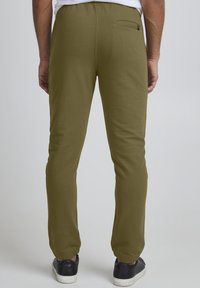 Olivgrüne Jogginghosen aus einem glatten Material mit elastischem Bund, schmal zulaufenden Beinen und einer Rückentasche, kombiniert mit dunklen Sneakern.