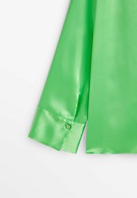Poignet à manches longues d'une chemise en satin vert vif avec une fermeture à un bouton sur un fond blanc.