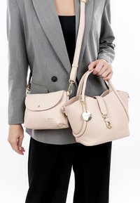 Due borse a tracolla color beige chiaro sono tenute da una persona. Una è una borsa a secchiello strutturata con dettagli in metallo dorato, l'altra è una borsa a patta con una finitura liscia.