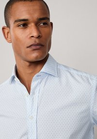 Camicia azzurro chiaro con bottoni, caratterizzata da un piccolo e discreto motivo a pois. Realizzata in tessuto morbido con colletto a punta e bottoni bianchi.