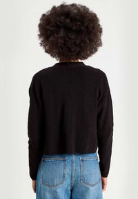 Svart kortad stickad tröja med långa ärmar, strukturvävt tyg och rund halsringning, bärs med ljusblå högmidjade jeans.
