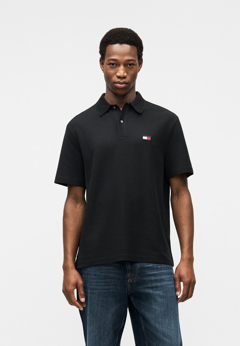 Μαύρο πόλο μπλουζάκι με γιακά, κατασκευασμένο από βαμβάκι. Διαθέτει μικρό, πολύχρωμο λογότυπο στο αριστερό στήθος. Φοριέται με μπλε τζιν, σε casual γραμμή.