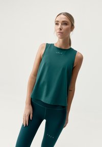 Top sportivo in verde scuro con scollatura a girocollo e vestibilità morbida. Presenta un logo discreto sul petto e leggings verdi coordinati.