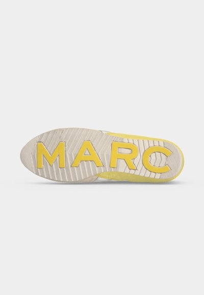 Semelle d'une chaussure jaune et beige avec les lettres M A R C en gros caractères jaunes au bas.