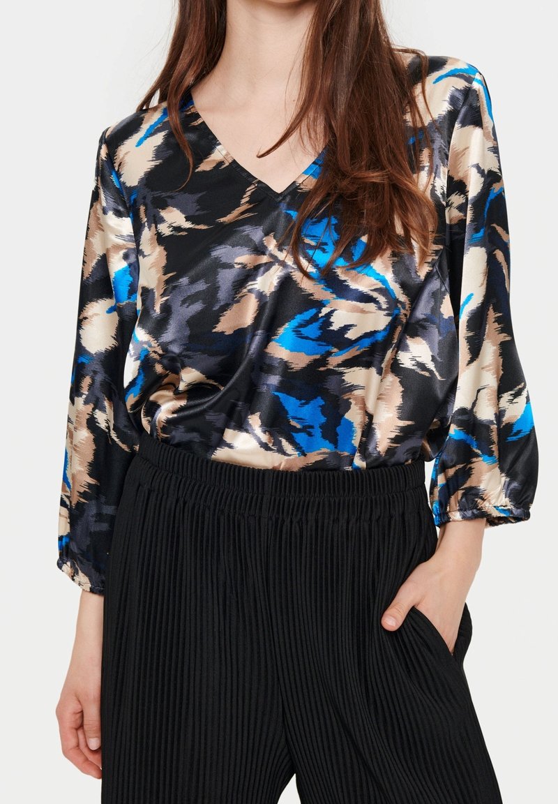 Satinblus med V-urt, med ett abstrakt mönster i svart, blått och beige. Matchas med svarta plisserade byxor.