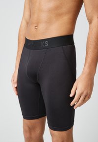 Boxer intimi aderenti neri con una texture liscia, caratterizzati da un ampio elastico nero goffrato con il nome del marchio. Hanno un design senza cuciture.