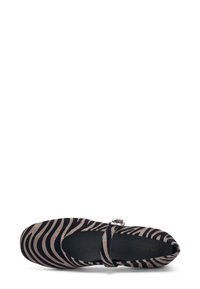 Zapato plano de rayas de cebra en negro y beige, con puntera redondeada, correa ajustable y parte superior de tela suave. Interior negro con un discreto detalle de logo.