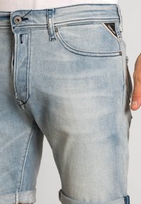 Şorturi din denim de culoare albastru deschis, cu un finisaj estompat, având un design clasic cu cinci buzunare, margini rulate și închidere cu un buton argintiu.