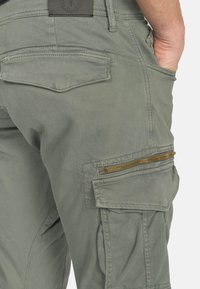 Olijfgroene cargobroek van katoenmix, met meerdere zakken, een ritssluiting zijzak met gouden hardware en een gestructureerde stofafwerking.