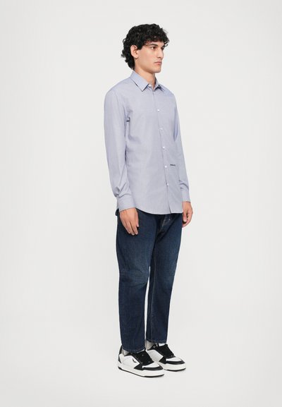 Langärmliges, hellblau karriertes Hemd mit Knöpfen und einer Brusttasche, kombiniert mit dunkelblauen Jeans und schwarz-weißen Sneakers.