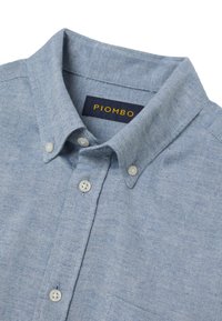 Camicia azzurro chiaro a spina di pesce con colletto button-down, con bottoni bianchi e etichetta PIOMBO blu navy all'interno del colletto.