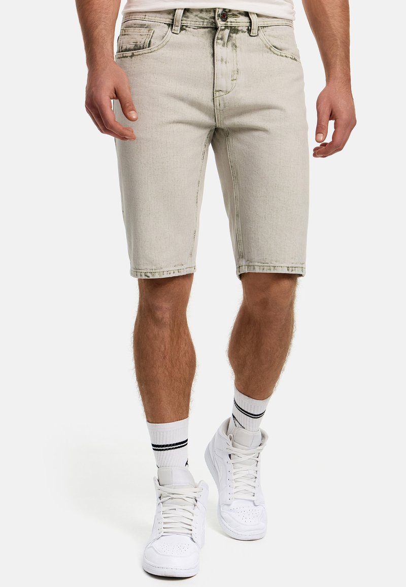 Lys grå denim shorts med lige skæring, fem lommer, frontknaplukning og synlige sømme. Bæres med hvide sneakers og stribede sokker.