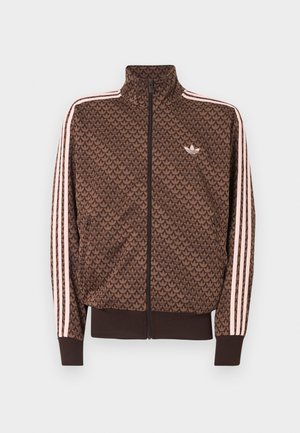 Καφέ αθλητικό μπουφάν Adidas με επαναλαμβανόμενο μοτίβο trefoil, ροζ τρεις ρίγες στα μανίκια, φερμουάρ μπροστά και μικρό λογότυπο trefoil στο στήθος.