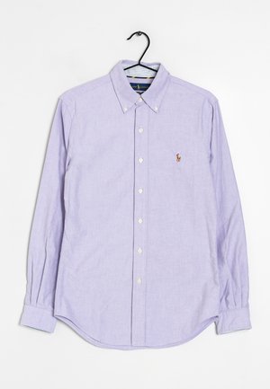 Jasnofioletowa, długorękawowa koszula na guziki z kołnierzykiem zapinanym na guziki oraz małym haftowanym logo na lewej piersi, wisząca na czarnym wieszaku.