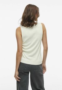 Top sin mangas de punto color crema con un diseño ajustado, tela texturizada y un acabado suave, combinado con jeans de pierna ancha en gris oscuro.