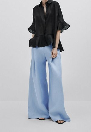 Czarna bluzka z peplum z krótkimi, falbaniastymi rękawami w połączeniu z szerokimi, miękkimi, niebieskimi spodniami. Lekka tkanina o gładkiej fakturze.