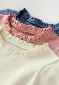 Drei Trikots mit Rüschensaum in Weiß, Pink und Marineblau. Weiches Baumwollmaterial mit feiner Textur und einem Schleifendetail auf dem weißen Oberteil.