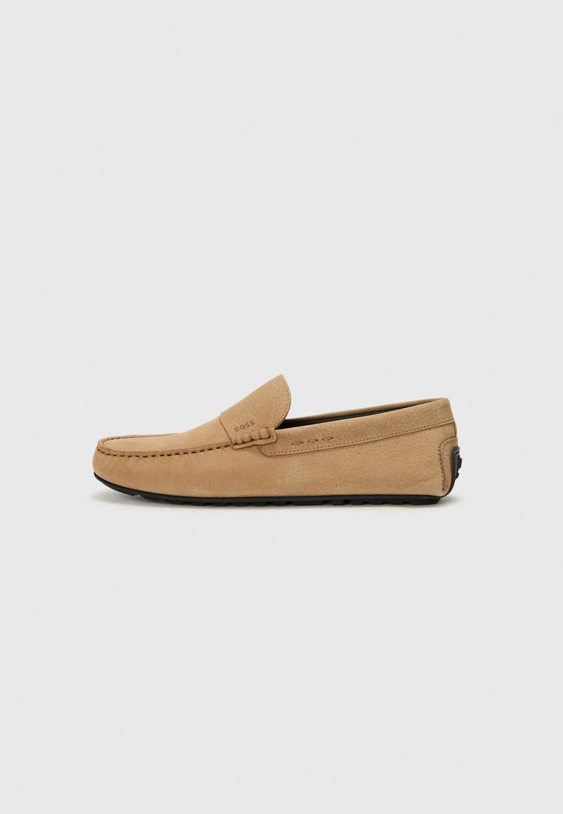 Mocasín de ante beige con puntera cosida, diseño sin cordones y suela de goma negra. Presenta un sutil logotipo en el lateral.