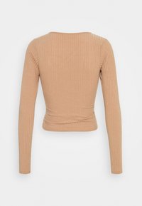 Långärmad ribbad topp i ljusbrun färg. Har en rund urringning och en åtsittande design, med texturerad tyg och en kortad silhuett.