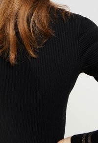 Pull noir côtelé avec une coupe ajustée et un tissu texturé. Accent remarquable de rayures dorées le long de la manche.