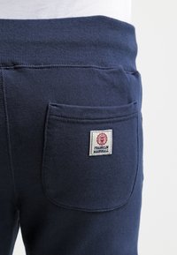 Mörkblå sweatpants i mjukt material har en bakficka med en röd och vit etikett som säger "FRANKLIN MARSHALL."