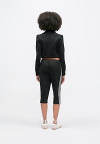 Μαύρο κοντό πουλόβερ με φουσκωτά μανίκια, σε συνδυασμό με μαύρο καπρί παντελόνι με λευκές ρίγες στο πλάι. Το άτομο φοράει μπεζ παπούτσια.