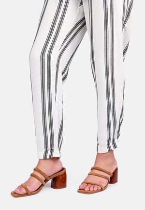 Sandali a blocco in suede beige con due sottili cinghie, abbinati a pantaloni bianchi leggeri con strisce verticali nere.