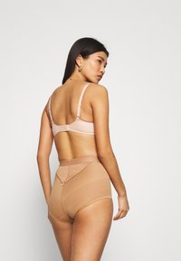 Nude bh med justerbare stropper og hægclosure, parret med højtaljede shaping shorts med en glat tekstur og en subtil ribbet mønster.