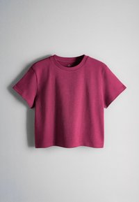T-shirt court manches courtes cropped rose profond uni suspendu sur un fond gris clair.