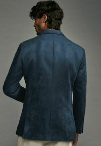 Blazer en daim bleu marine au toucher lisse, avec une fente unique à l'arrière et des épaules structurées, doté de longues manches et d'une coupe ajustée.