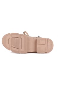 Suela de zapato de goma color beige con agarre texturizado, que presenta un tacón grueso y un patrón de diseño elevado. Incluye un bucle para facilitar su uso.