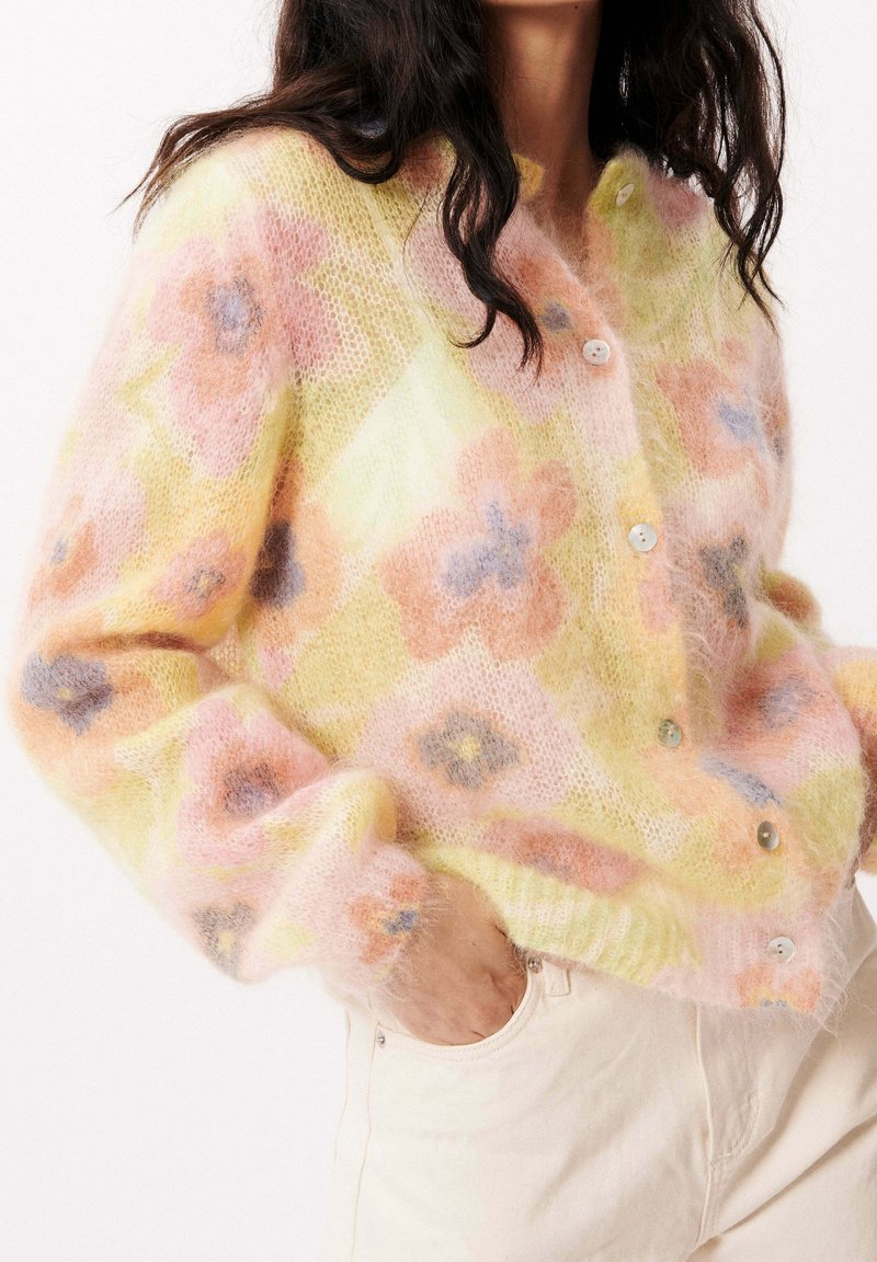 Pastel floral cardigan in soft, fluffy knit. Features orange and blue flowers on a yellow background, with rounded buttons and ribbed hem.