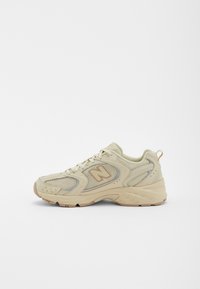 Béžová síťovaná atletická obuv s polstrovanou podrážkou, flexibilním designem a decentními stříbrnými akcenty. Lehké provedení a systém šněrování.