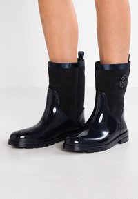 Mustat patenttinahasta ja mokasta tehdyt nilkkurit, joissa on pyöreä kärki, sileä pinta, kiiltävä viimeistely ja sivussa oleva logoyksityiskohta.