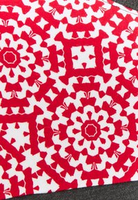 Tela roja y blanca con un patrón floral geométrico, que consiste en motivos circulares y acentos angulares, sobre una superficie texturizada.