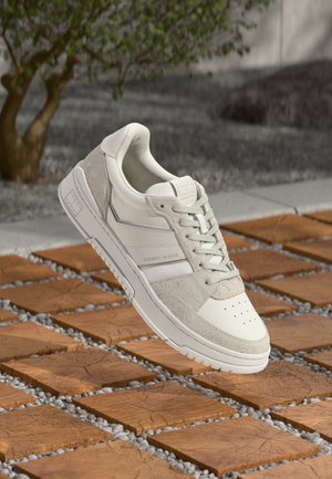 White and gray sneakers with a smooth leather upper, textured suede accents, and perforated toe. Features a logo and flat laces.