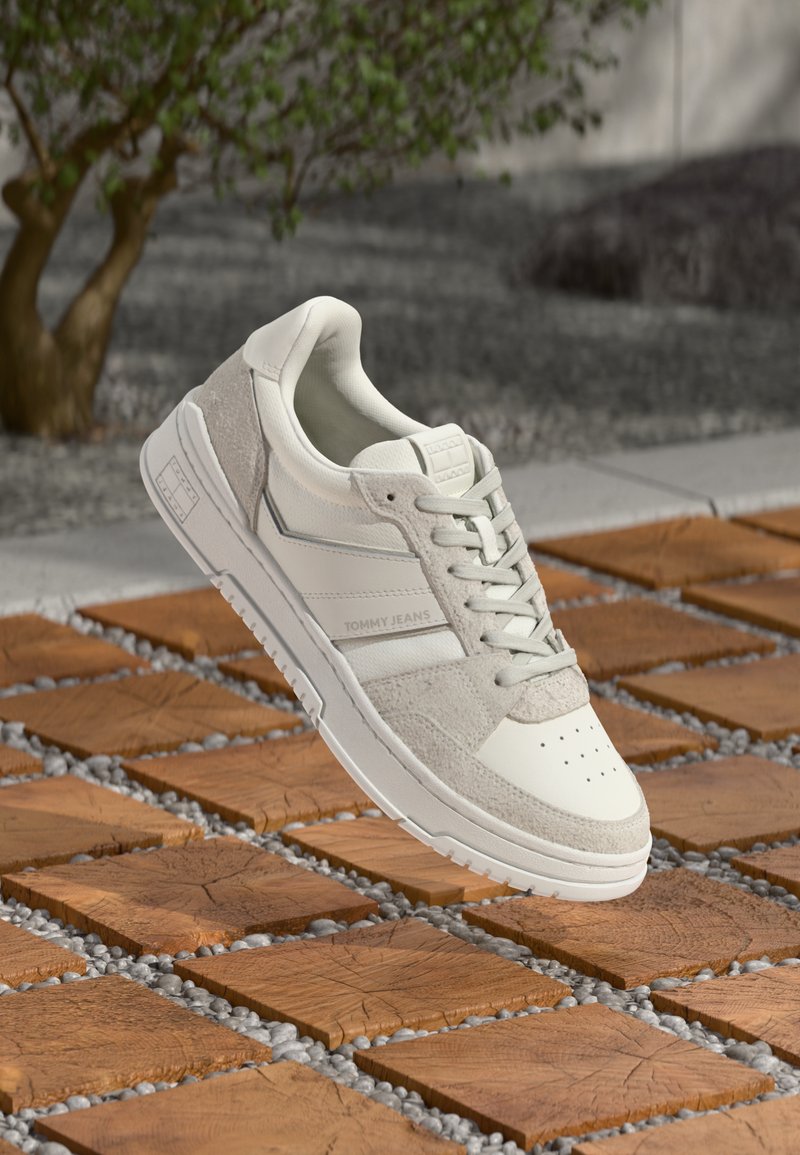 White and gray sneakers with a smooth leather upper, textured suede accents, and perforated toe. Features a logo and flat laces.