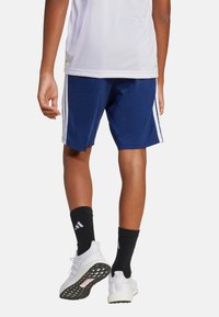 Pantalones cortos deportivos de la Marina con franjas laterales blancas, hechos de un tejido suave. Combinados con calcetines negros y zapatillas blancas con suelas texturizadas.