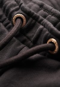Joggers noirs en coton avec une taille texturée, dotés d'œillets en bronze et d'un cordon de serrage pour un ajustement réglable.