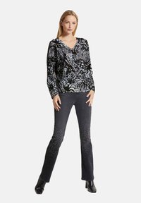 Schwarzes Langarmoberteil mit weißen abstrakten Mustern, kombiniert mit dunklen Jeans, die verstreute Strasssteine aufweisen. Die Jeans haben einen eng anliegenden Schnitt.