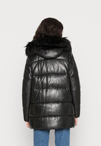 Černá kožená péřová bunda s kapucí z umělé kožešiny, která má prošívané části a volný střih. Záda neobsahují viditelné zapínání.