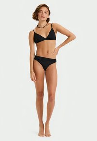 Set de bikini negru, compus dintr-un top bralette triunghiular cu bretele subțiri și fund aproximativ la bătaie. Textură netedă cu un design minim.