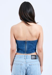 Top bandeau z denimu w ciemnoniebieskim kolorze o zorganizowanej strukturze, z zamkiem błyskawicznym z tyłu. W połączeniu z jasnoniebieskimi, wysokim stanem dżinsami.