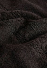 Tmavá vlněná tkanina s textúrovaným tkaným vzorom, ktorá má jemné záhyby a mäkký, chlpatý povrch. Bohatá čierna farba s jemnou hĺbkou.