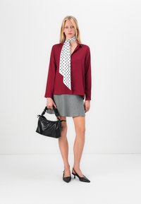 Burgundy blus med knappar, prickig scarf, grå kjol och svart texturerad handväska. Svarta slingbacks med spetsiga tår fulländar outfiten.